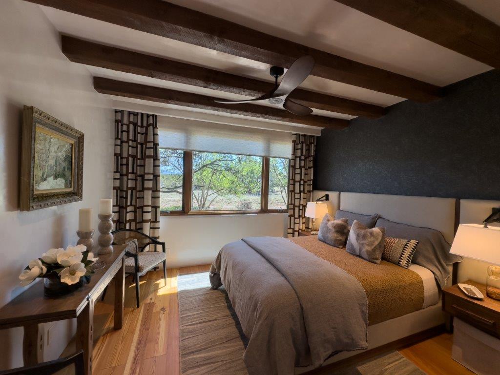 Final-Hirez-Stoilis-Arrowhead-BedroomIMG_2126-3 santa fe style bedroom in Las Campanas, window with drapey on back wall, dark wall behind headboard, wooden flooring, muted colors and rugs